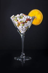 Pills in cocktail glass in front of a black background with a shiny orange slice