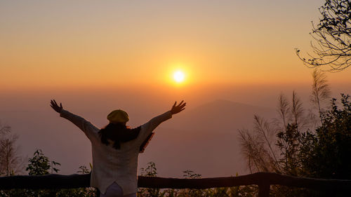 Rear view of woman with arms outstretched standing against sky during sunrise