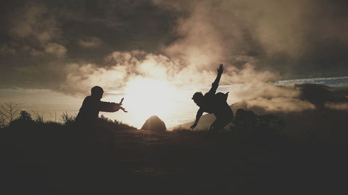 Silhouette friends playing on field against sky during sunset