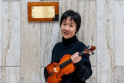 Young chinese female violin maker showing her freshly made violin outdoors in front of her workshop