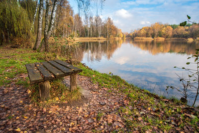 Bench by lake against sky during autumn