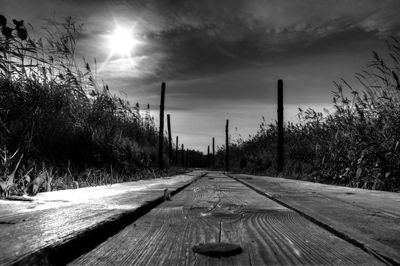 Empty boardwalk amidst field against sky