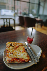 High angle close-up of pizza slice in plate on wooden table at restaurant