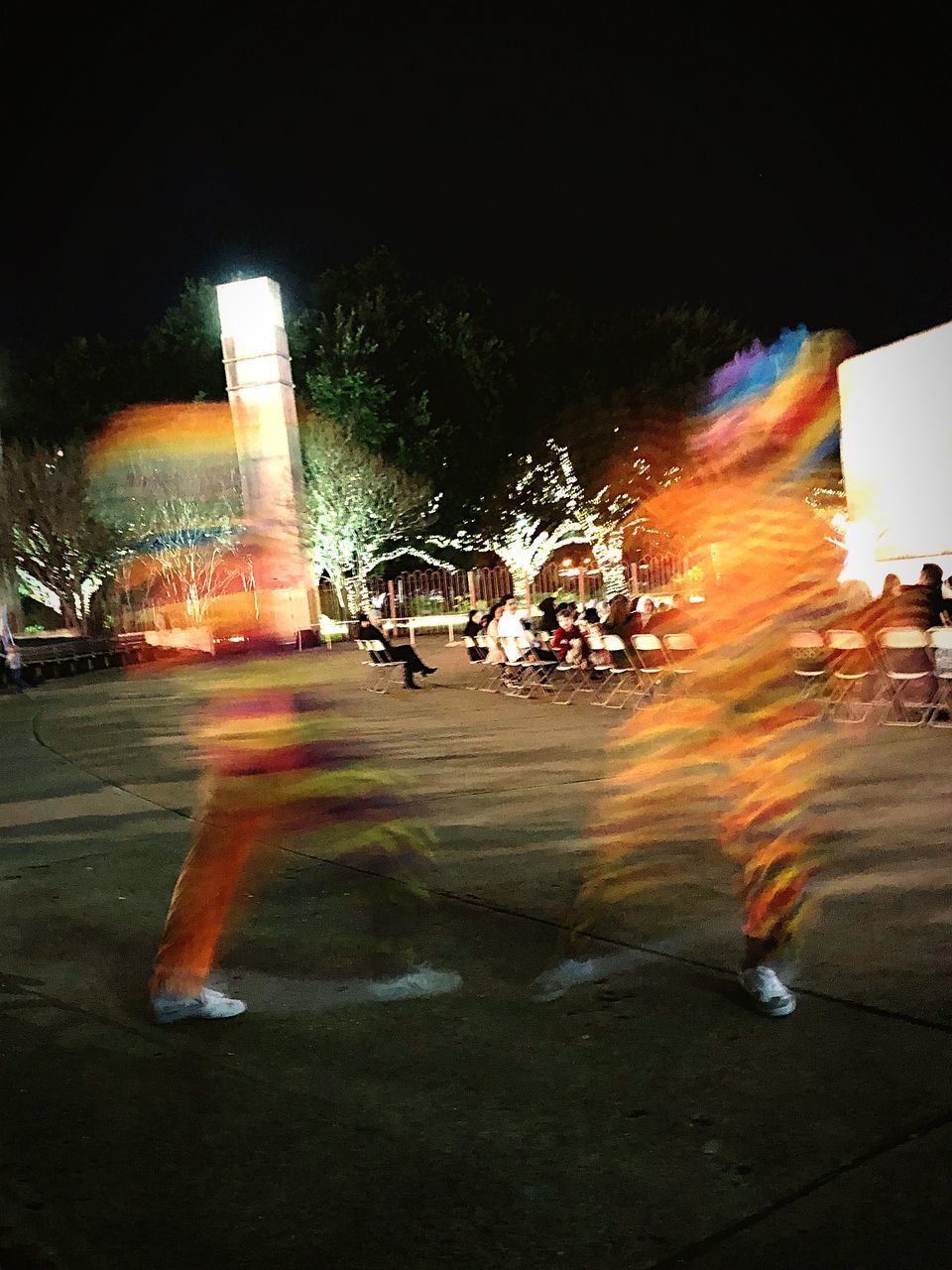 BLURRED MOTION OF PEOPLE AGAINST ILLUMINATED ROAD AT NIGHT