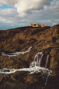 Water flowing on rock formations against sky