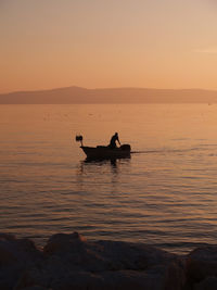 Silhouette man in boat on sea at sunset