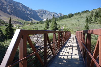 Footbridge leading towards mountains against clear sky