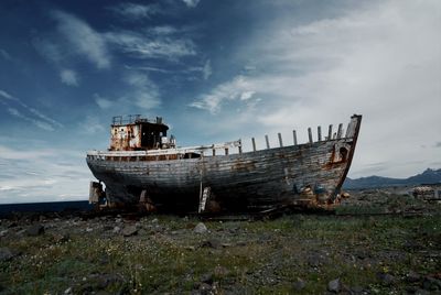 Abandoned boat on field against sky