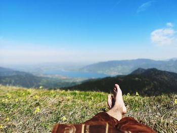 Low section of man lying on field against sky during sunny day