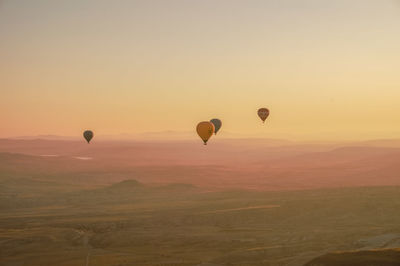 Hot air balloons flying over landscape against sky during sunset