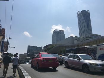 Cars on road by buildings in city against sky