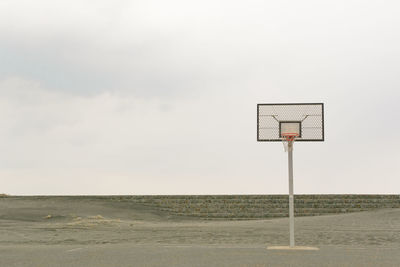 Basketball hoop on court at beach against cloudy sky