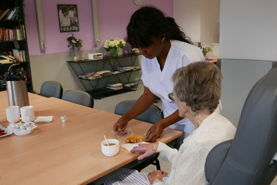 Caretaker serving breakfast to senior woman in nursing home