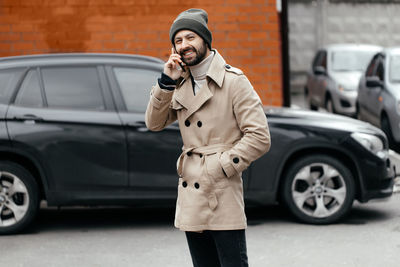 Portrait of smiling man talking on phone against car