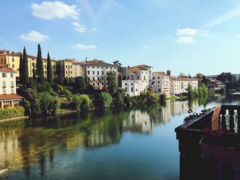 Buildings by river against sky in city