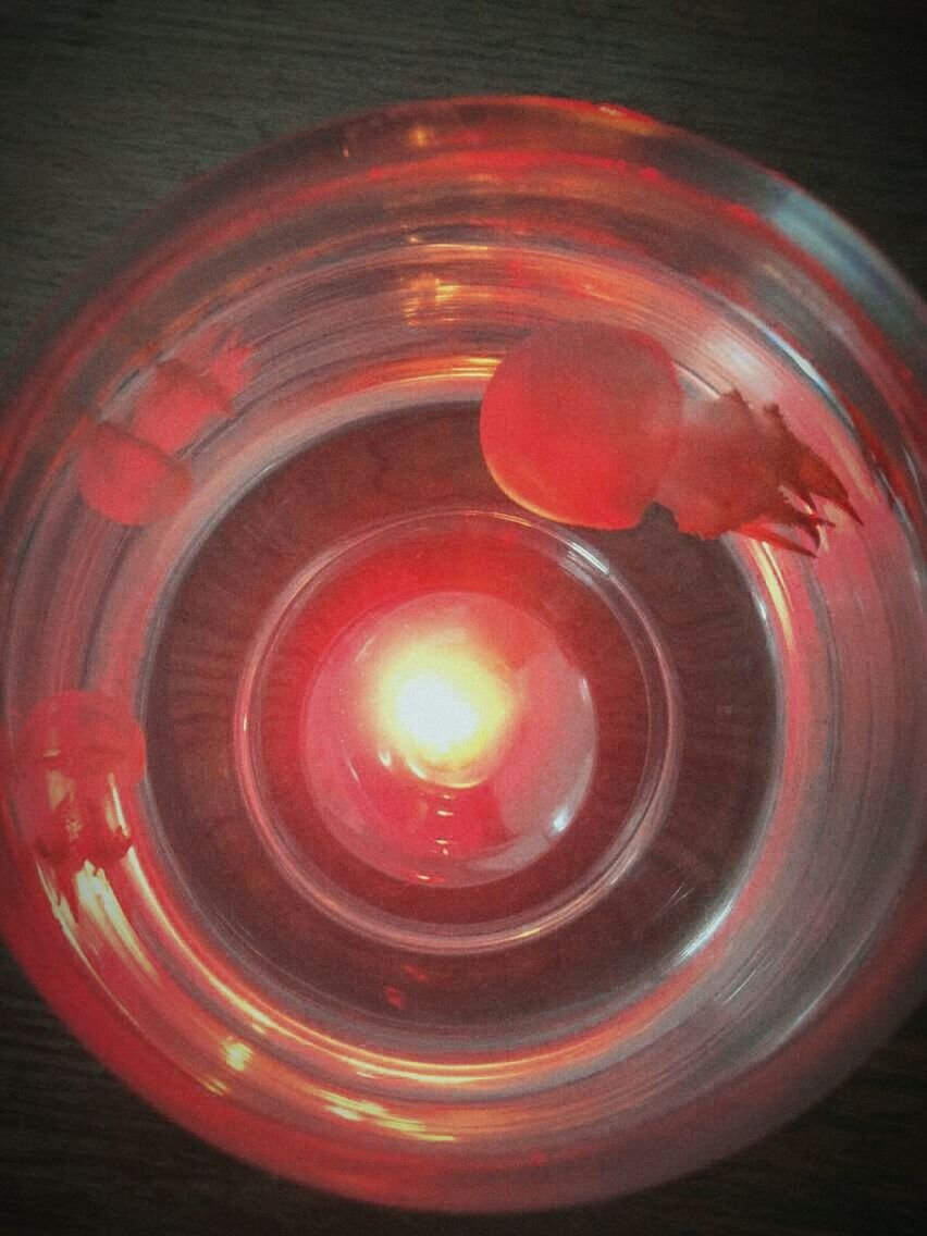 indoors, red, illuminated, close-up, circle, high angle view, glowing, still life, glass - material, table, burning, no people, lighting equipment, pattern, transparent, orange color, flame, fire - natural phenomenon, reflection, candle