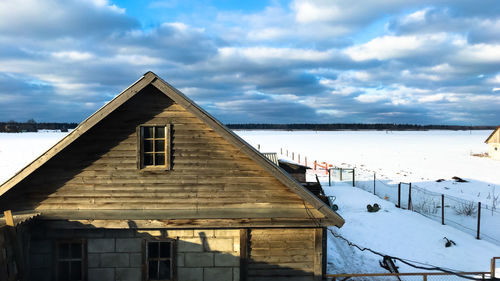 Snow covered house by building against sky