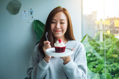 A beautiful asian woman holding and eating a red velvet cupcake