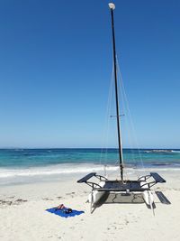 Outrigger boat at beach against clear blue sky