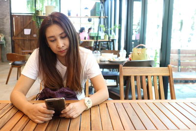 Young woman using phone while sitting on table