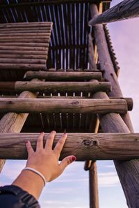 Cropped hand of woman climbing on ladder against sky