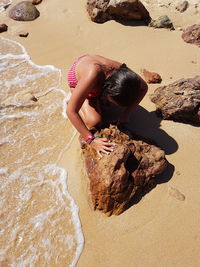 High angle view of girl crouching by rock on shore at beach