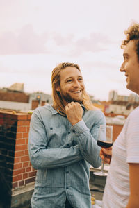 Smiling male friends talking while standing on terrace at rooftop party