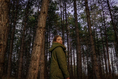 Young woman standing by tree trunk in forest