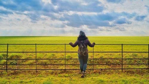 Rear view of woman standing by fence on land