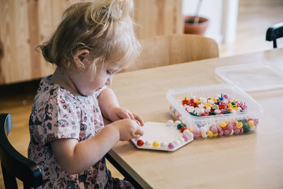 Blond girl playing with pegboard game on table at home