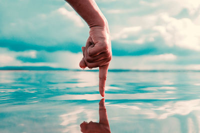 Close-up of mans pointing finger in water against sky