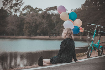 Side view of woman with colorful balloons looking at lake during sunset