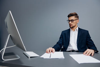 Portrait of businessman using laptop while standing against wall