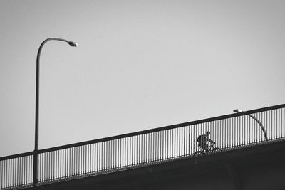 Low angle view of man riding bicycle on bridge against clear sky