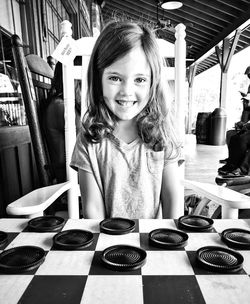 Portrait of smiling girl playing checkers at porch