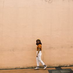 Full length of young woman walking on sidewalk by wall