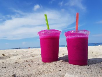 Close-up of pink juice on beach against blue sky