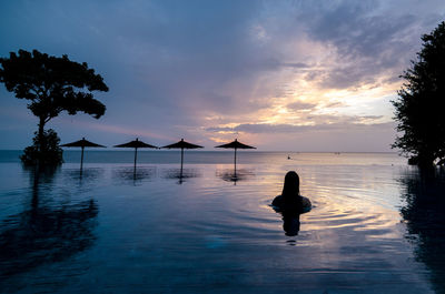 Silhouette person in swimming pool against sky during sunset