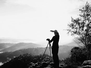 Photographer works on cliff.  dreamy fogy landscape, spring misty sunrise in beautiful valley below.