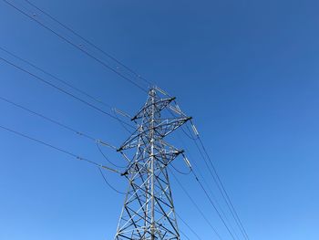 Low angle view of electricity pylon against blue sky