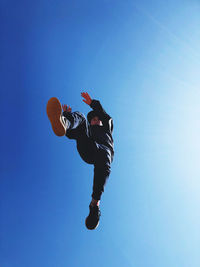 Low angle view of person jumping against blue sky