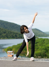 Teenage girl exercising on roadside against sky