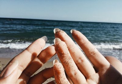 Cropped image of hand on sea shore against sky