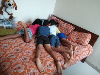 Rear view of friends using laptop while lying on bed at home