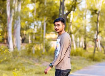 Portrait of young man standing on road against trees