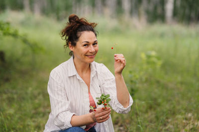 Woman in casual clothes picking forest strawberry in summer woods