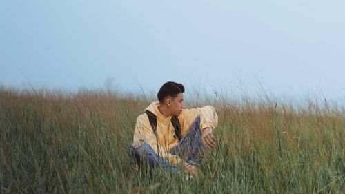 Young man sitting on field against clear sky