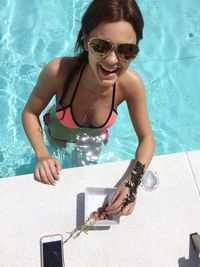 High angle view of young woman in sunglasses eating grape while standing in pool