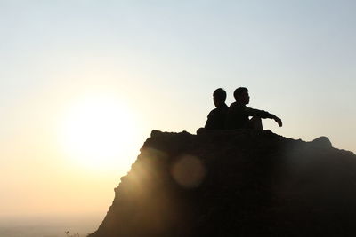 Silhouette man sitting on rock against sky during sunset