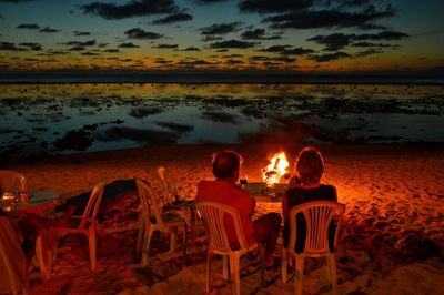 Rear view of people sitting on beach at sunset